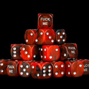 May include: A pyramid-shaped stack of red and black marbled dice against a black background. Several dice feature the text FUCK ME in silver lettering, while others display standard white pips. The dice are arranged in a tiered formation.