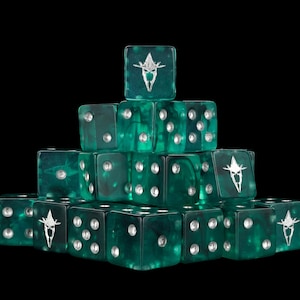 Peut inclure: Une pile pyramidale de dés à six faces en vert émeraude translucide. Chaque dé présente des points argentés et un emblème personnalisé argenté sur une face, représentant un motif de crâne ou de casque à cornes stylisé sur fond sombre.