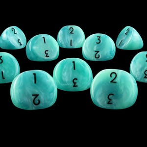 May include: A collection of ten smooth, rounded, turquoise and white marbled gaming pieces. Each piece features a distinct, black printed numeral, specifically the numbers one, two, and three, arranged in various orientations across the surfaces.