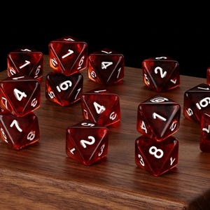 May include: A collection of translucent dark red polyhedral dice with white numbers. The dice are multi-sided shapes, including d20s, d12s, d10s, d8s, d6s, and d4s, scattered across a smooth, polished wooden surface with a visible grain pattern.