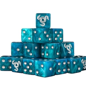 Könnte beinhalten: Eine Pyramide aus türkisblauen Würfeln mit silbernen Augen und Drachendesigns. Die Würfel sind in einer gestapelten Formation angeordnet, die ihr marmoriertes Aussehen zeigt. Jeder Würfel hat ein Drachenemblem.