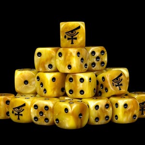 May include: A pyramid stack of yellow marbled dice against a black background. Each die features black pips representing numbers, while some faces display a black graphic of an eye above an ankh symbol. The dice have a smooth, polished finish.