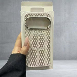 May include: A white smartphone case featuring a perforated mesh pattern across the back, a circular magnetic charging ring, and a metallic silver horizontal camera cutout, presented inside its original white cardboard retail packaging.