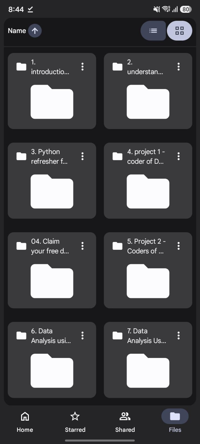 K&ouml;nnte beinhalten: Eine mobile Benutzeroberfl&auml;che mit einem Raster aus acht dunkelgrauen Ordnersymbolen, die mit Texten wie Introduction, Understanding, Python refresher, Project 1, Claim your free, Project 2 und Data Analysis beschriftet sind, sowie Navigationssymbolen.