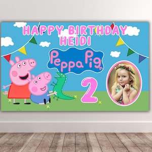 Pode incluir: Uma faixa de aniversário retangular com fundo de céu azul claro, nuvens brancas e bandeirolas coloridas. Exibe o texto HAPPY BIRTHDAY HEIDI, o logotipo da Peppa Pig, um dinossauro verde, um grande número 2 rosa e a foto de uma criança.