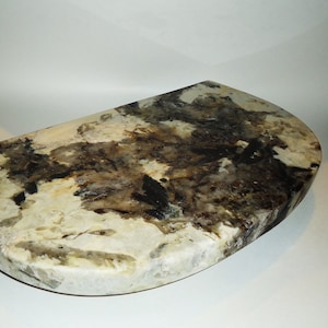 May include: A half-round shelf made of white and brown granite with a mottled pattern. The shelf has a smooth, polished surface.