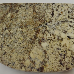 May include: A close-up of a light brown, beige, and gray granite countertop with a rounded edge.