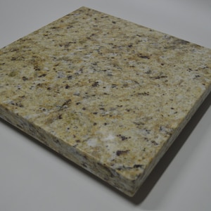 May include: A square tile of polished granite with a light brown and beige color with dark brown flecks throughout.