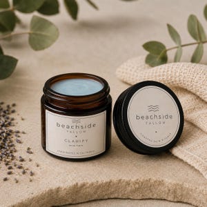 Könnte beinhalten: Ein bernsteinfarbenes Glas mit Clarify Aknebalsam und hellblauer Creme. Das weiße Etikett trägt die Aufschrift beachside TALLOW CLARIFY acne balm HANDCRAFTED IN CALIFORNIA. Der schwarze Deckel daneben zeigt den Text beachside TALLOW COASTAL SKIN RITUALS.