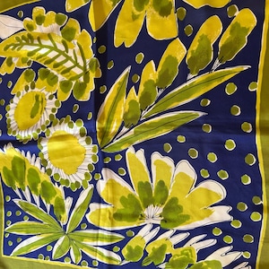 May include: A square silk scarf with a floral design. The scarf features large yellow and white flowers, green leaves, and a navy blue background with small white dots. The border is a solid green.