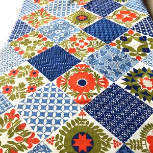May include: A colorful patchwork fabric with a variety of floral and geometric patterns. The design features squares in shades of blue, orange, green, and white. The fabric is likely used for quilting or home decor projects.