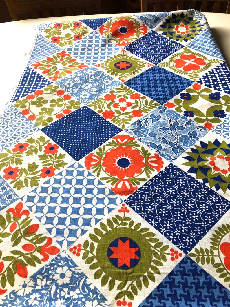 May include: A colorful patchwork fabric with a variety of floral and geometric patterns. The design features squares in shades of blue, orange, green, and white. The fabric is likely used for quilting or home decor projects.
