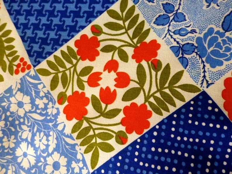 May include: Close-up of a patchwork fabric with various patterns. The design includes squares with floral, polka dot, and geometric patterns in shades of red, blue, green, and white. The fabric has a vintage aesthetic.