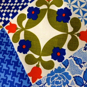 May include: Close-up of a fabric with a patchwork design. The fabric features various geometric and floral patterns in blue, red, green, and white. The patterns include stylized flowers, geometric shapes, and floral motifs, creating a vibrant and colorful textile.