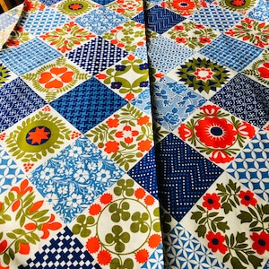 May include: A colorful fabric with a patchwork design. The fabric features a variety of geometric and floral patterns in shades of blue, orange, green, and white. The fabric is labeled "Waverly Fabrics".