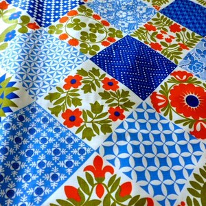 May include: A patchwork textile featuring a variety of geometric and floral patterns in shades of blue, white, orange, and green. The design includes squares with stylized flowers, dots, and geometric shapes, creating a vibrant and colorful display.