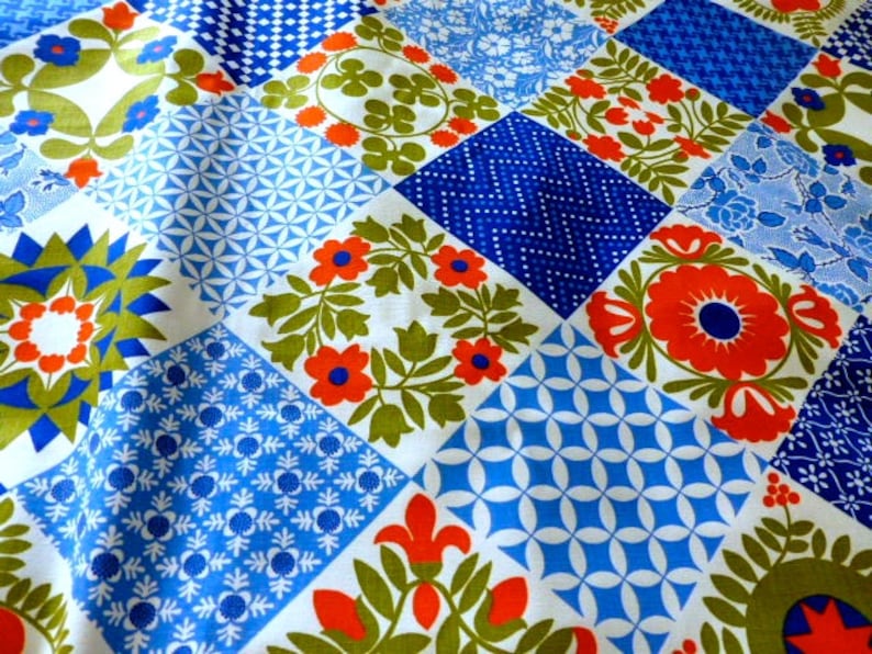 May include: A patchwork textile featuring a variety of geometric and floral patterns in shades of blue, white, orange, and green. The design includes squares with stylized flowers, dots, and geometric shapes, creating a vibrant and colorful display.