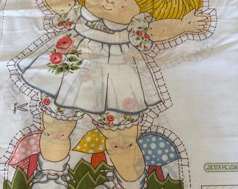 May include: A vintage Cabbage Patch Kids fabric panel featuring a doll illustration. The doll has blonde pigtails with pink bows, a white dress with floral accents, and is standing in a garden scene with mushrooms and flowers.