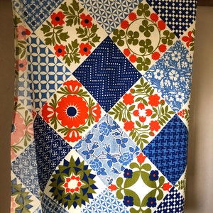 May include: A vintage fabric with a patchwork design. The fabric features a variety of geometric and floral patterns in shades of blue, red, green, and white. The fabric is labeled "Protected with Scotchgard".