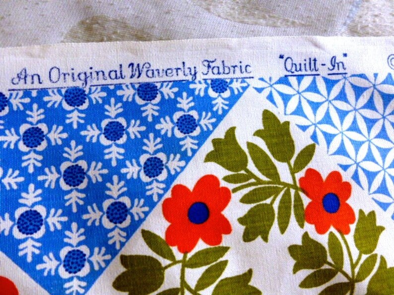 May include: Close-up of a fabric swatch with a floral and geometric pattern. The fabric features red flowers with blue centers, green leaves, and blue and white geometric shapes. The text "An Original Waverly Fabric" and "Quilt-In" is printed on the fabric.