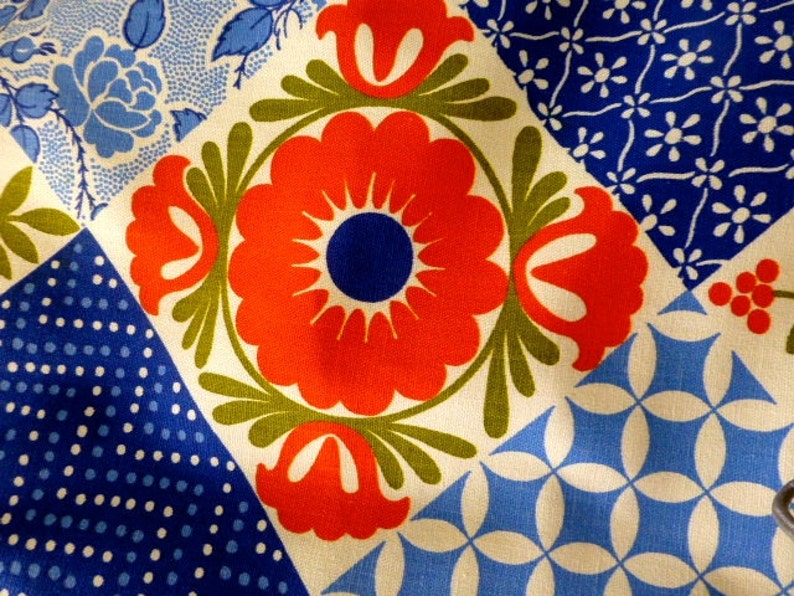 May include: Close-up of a fabric with a patchwork design. The design features a large red flower with a blue center, surrounded by green leaves. Other squares have blue floral and polka dot patterns on a white background.