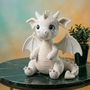 Peut inclure: Un dragon blanc crochet&eacute; avec de grands yeux bleus, des ailes et des cornes. La cr&eacute;ature fantastique faite &agrave; la main est assise sur une table en marbre vert. Le dragon est une sculpture douce, parfaite pour une chambre d'enfant ou comme cadeau unique.