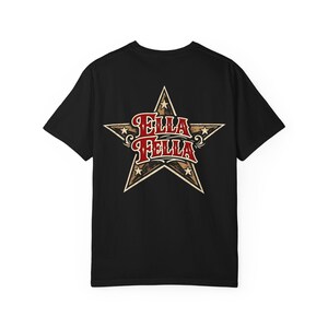 Puede incluir: Una camiseta negra de manga corta con un gran gráfico en la espalda. El diseño consiste en una estrella beige y marrón con textura desgastada, que contiene el texto rojo ELLA FELLA en una fuente audaz y estilizada con bordes blancos.