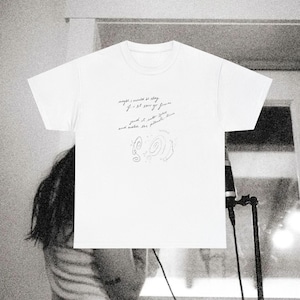 May include: A white short-sleeve t-shirt featuring black cursive text that reads, "maybe i would be okay if i let this go forever, send it into space and watch the planets turn," accompanied by a small line drawing of a spiral galaxy.