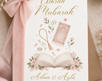 May include: A white greeting card featuring the gold text Umrah Mubarak and Adam & Ayla with the phrase May Allah SWT accept your umrah & reward you for your efforts. The card displays watercolor illustrations of a prayer mat, beads, and flowers.