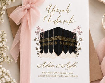 May include: A white greeting card featuring the text Umrah Mubarak in gold script, an illustration of the black and gold Kaaba, and the names Adam & Ayla. Below is the text May Allah SWT accept your umrah & reward you for your efforts. A soft pink ribbon is tied to the left side of the card.