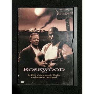 May include: A DVD case for the film Rosewood featuring two men in the foreground, one holding a firearm. The background shows a town under a dark sky with smoke. The title Rosewood is printed in white, with the text In 1923, a black town in Florida was burned to the ground.