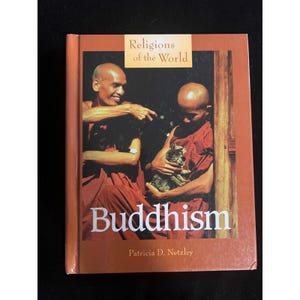 May include: A hardcover book titled Religions of the World: Buddhism by Patricia D. Netzley. The cover features a photograph of two individuals in red robes holding cats, with the title text in white and a tan rectangular header at the top.