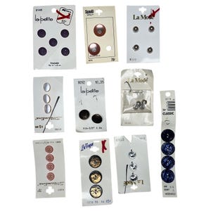 May include: A collection of various buttons on their original cards. The buttons are in different colors, shapes, and sizes. Some cards have text like "La Mode" and "la-petite".