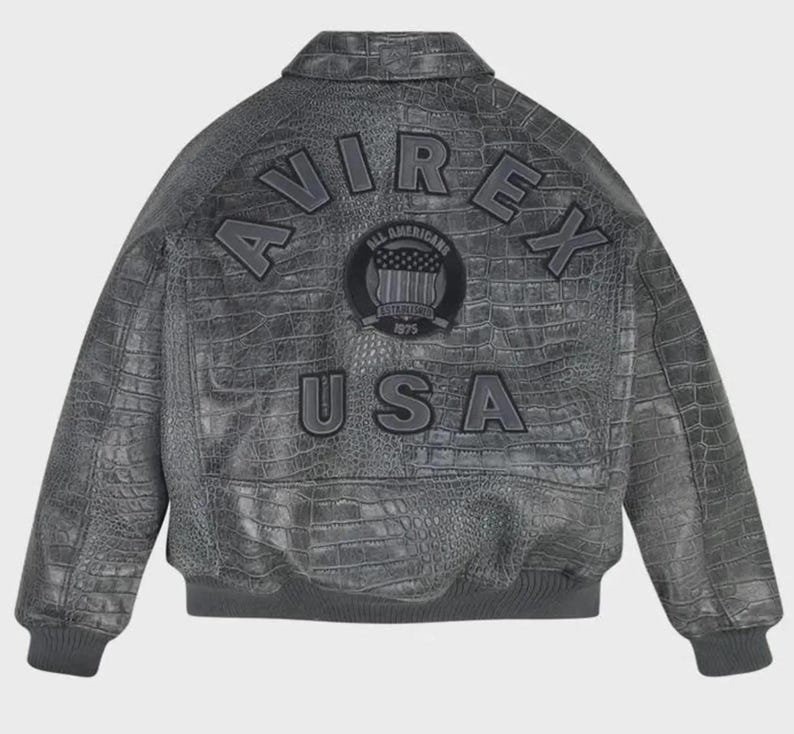May include: A charcoal grey jacket with a textured crocodile skin pattern. The back features the text AVIREX in an arched design, the text USA below it, and a circular patch in the center with the text ALL AMERICANS ESTABLISHED 1975.