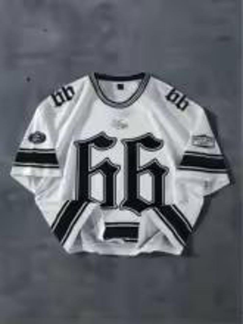 May include: White short-sleeve jersey with black accents and the number "66" prominently displayed on the front. The jersey features black stripes on the sleeves and collar, with additional text and logos. The jersey is laid flat on a gray surface.