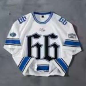 May include: White jersey with blue and black accents, featuring the number "66" in large, gothic-style font on the front. The jersey has blue stripes on the sleeves and collar, with patches on the sleeves. The jersey is displayed on a gray surface.