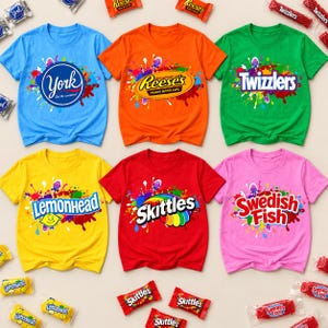 May include: Six short-sleeved t-shirts in blue, orange, green, yellow, red, and pink, each featuring a colourful paint splatter design and a candy brand logo: York, Reese's, Twizzlers, Lemonhead, Skittles, and Swedish Fish, with matching sweets.