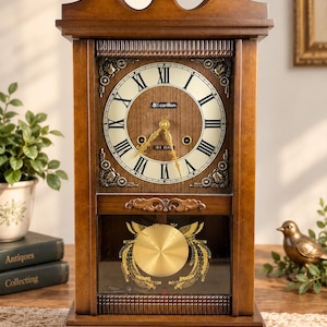 May include: A wooden mantel clock with a dark brown finish, featuring a cream-colored dial with black Roman numerals and the text carillon. The clock includes gold-colored hands and a circular brass pendulum visible behind a glass panel.