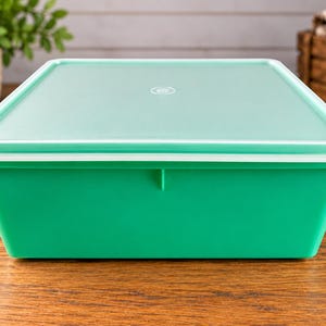 Peut inclure: Un récipient de stockage rectangulaire avec une base vert vif et un couvercle vert menthe plus clair. Le couvercle présente un petit logo circulaire centré. Le récipient a un dessus large et plat ainsi que des côtés légèrement inclinés.