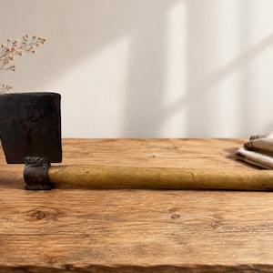 May include: A hand tool featuring a dark, weathered metal blade with a flat, rectangular edge attached to a long, cylindrical wooden handle. The metal head shows signs of oxidation and wear, while the wooden handle has a smooth, light brown finish.