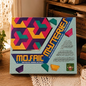 Peut inclure: Une boîte de jeu carrée intitulée Mosaic Mysteries, une activité de conception avec des blocs à motifs. La boîte présente une mosaïque géométrique colorée de formes roses, violettes, jaunes et sarcelle sur un fond bleu clair.