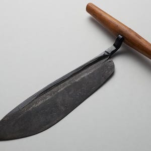 Peut inclure: Un couteau de style ancien et sombre avec une longue lame incurvée et un manche en bois. La lame est de couleur gris foncé et le manche est brun clair. Le couteau est conçu pour couper et trancher.