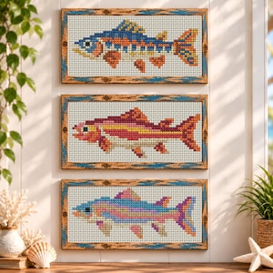 May include: Three rectangular framed cross-stitch artworks featuring fish designs. The top frame shows a blue and orange fish, the middle frame displays a pink and yellow fish, and the bottom frame depicts a multi-colored pastel fish.