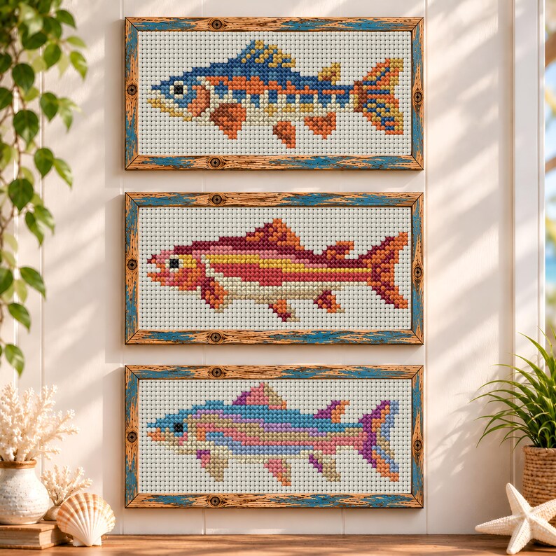 May include: Three rectangular framed cross-stitch artworks featuring fish designs. The top frame shows a blue and orange fish, the middle frame displays a pink and yellow fish, and the bottom frame depicts a multi-colored pastel fish.
