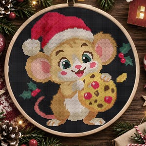 Op de afbeelding: Een kruissteekborduurwerk in een ronde houten ring met een beige muis met grote oren en roze wangen die een rode kerstmuts draagt. De muis houdt een geel koekje met rode en bruine stippen vast tegen een zwarte achtergrond met hulsttakjes.