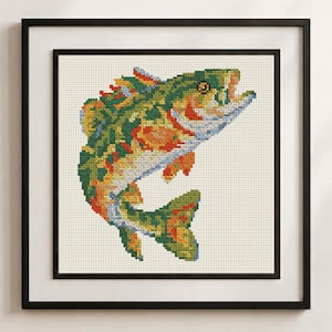 May include: A framed cross-stitch embroidery featuring a colorful fish in shades of green, orange, yellow, and blue. The fish is depicted in a leaping position against a cream-colored fabric background, enclosed within a simple black frame.