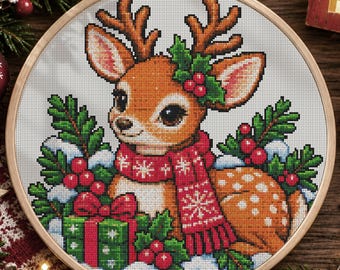 May include: A cross-stitch embroidery project in a round wooden hoop featuring a brown fawn with white spots, wearing a red scarf with white snowflake patterns. The fawn is surrounded by green holly leaves, red berries, and a green gift box.
