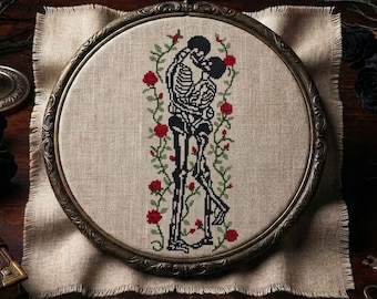 May include: A circular embroidery hoop containing a cross-stitch design of two skeletons embracing, surrounded by green vines and red roses. The embroidery is stitched onto a light beige fabric with frayed edges, held within an ornate bronze frame.