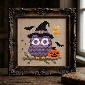 May include: A cross-stitch embroidery featuring a purple owl wearing a black witch hat, perched on a brown branch next to an orange jack-o'-lantern. The design includes a yellow crescent moon and two black bats on a beige fabric background.