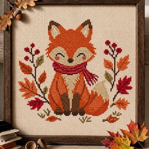May include: A cross-stitch embroidery of a fox wearing a red scarf, centered on beige fabric. The fox is surrounded by red berries and colorful autumn leaves in shades of orange, red, and green. The piece is enclosed in a dark wooden frame.